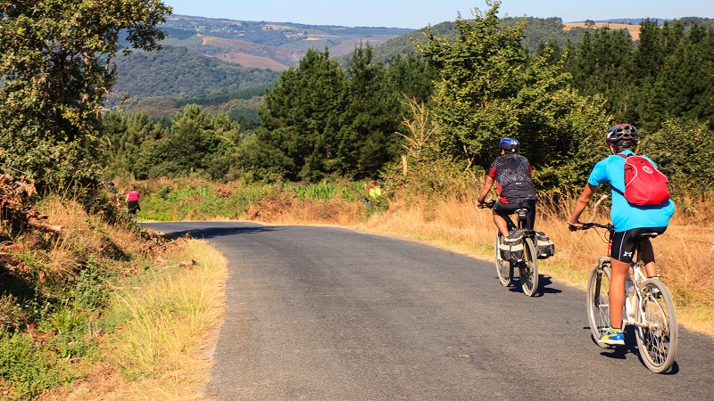 Två cyklister cyklar nerför en backe i kuperade, skogsklädda omgivningar.